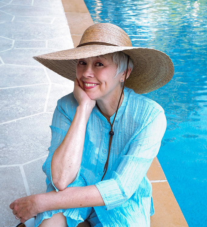 Woman in a blue cover-up and wide-brimmed hat by a pool. model