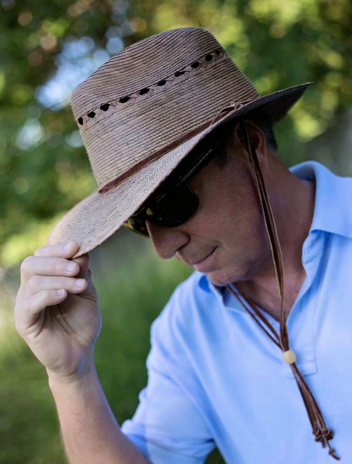 Man wearing a straw hat and sunglasses with a blurred natural background