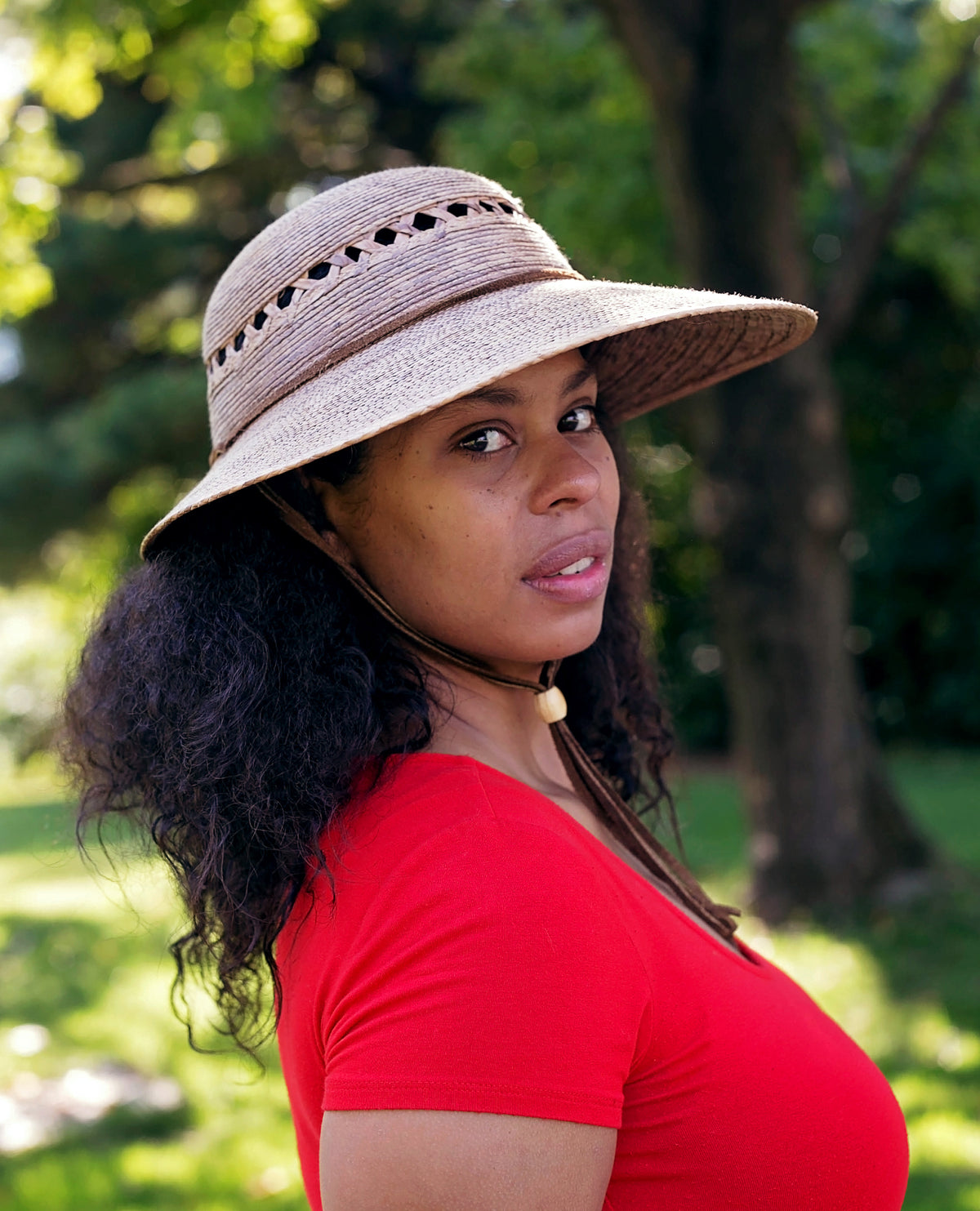 Model wearing a hand-woven Laurel Lattice Straw Hat with a wide brim, lattice cutouts, and leather chin strap.