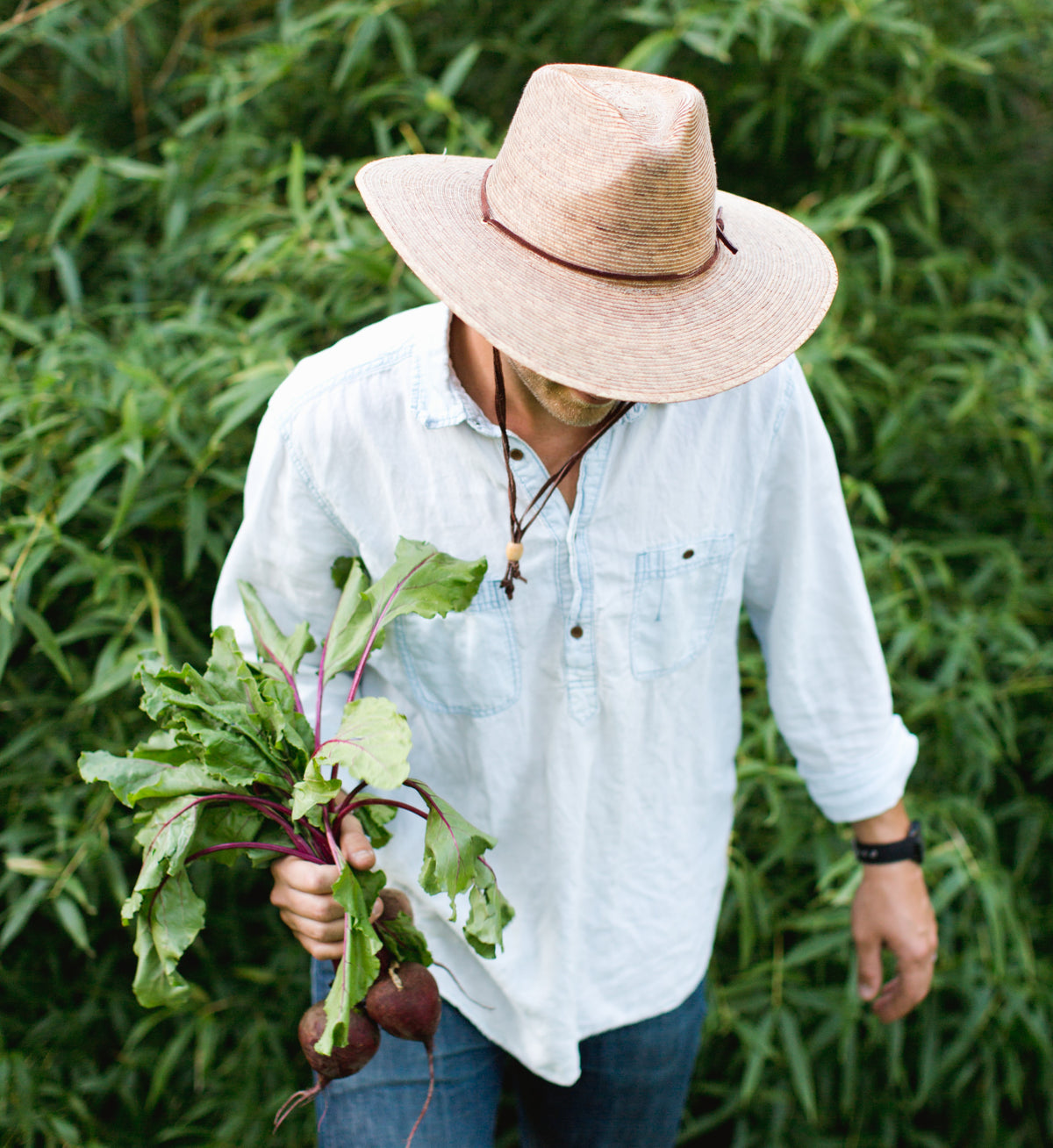 Gardener model in a wide-brimmed, natural palm straw hat with a brown chinstrap, holding beets.