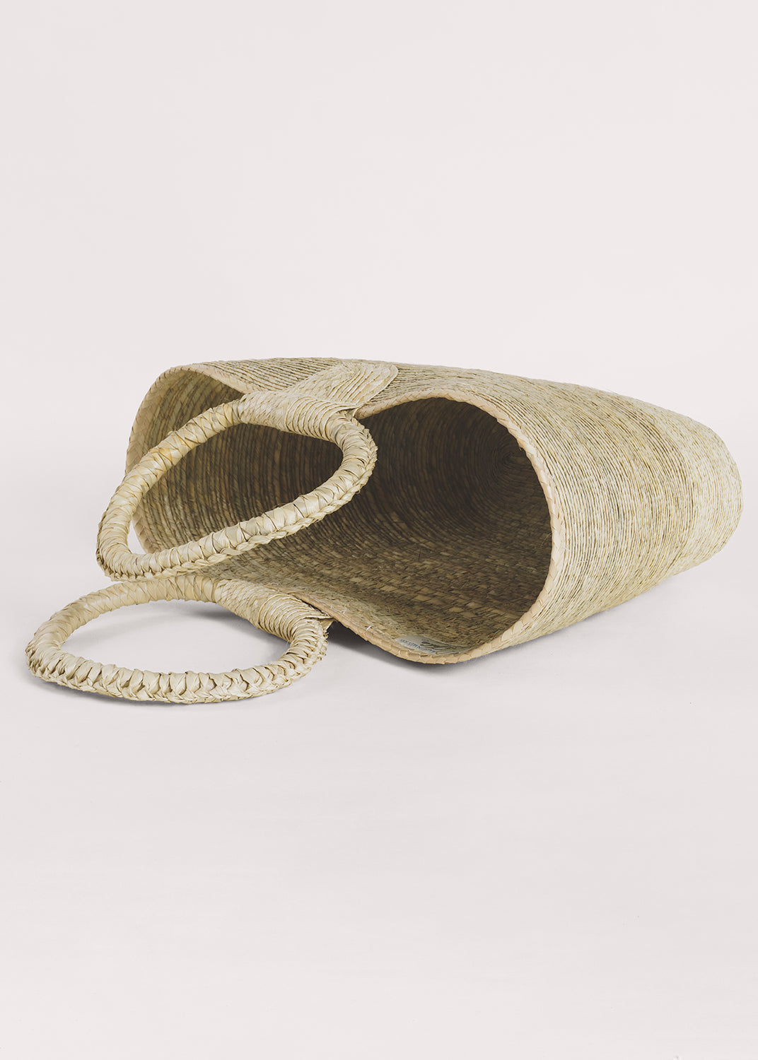 Light palm straw hand-woven tote with circular handles, lying on its side.