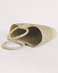 Light palm straw hand-woven tote with circular handles, lying on its side.