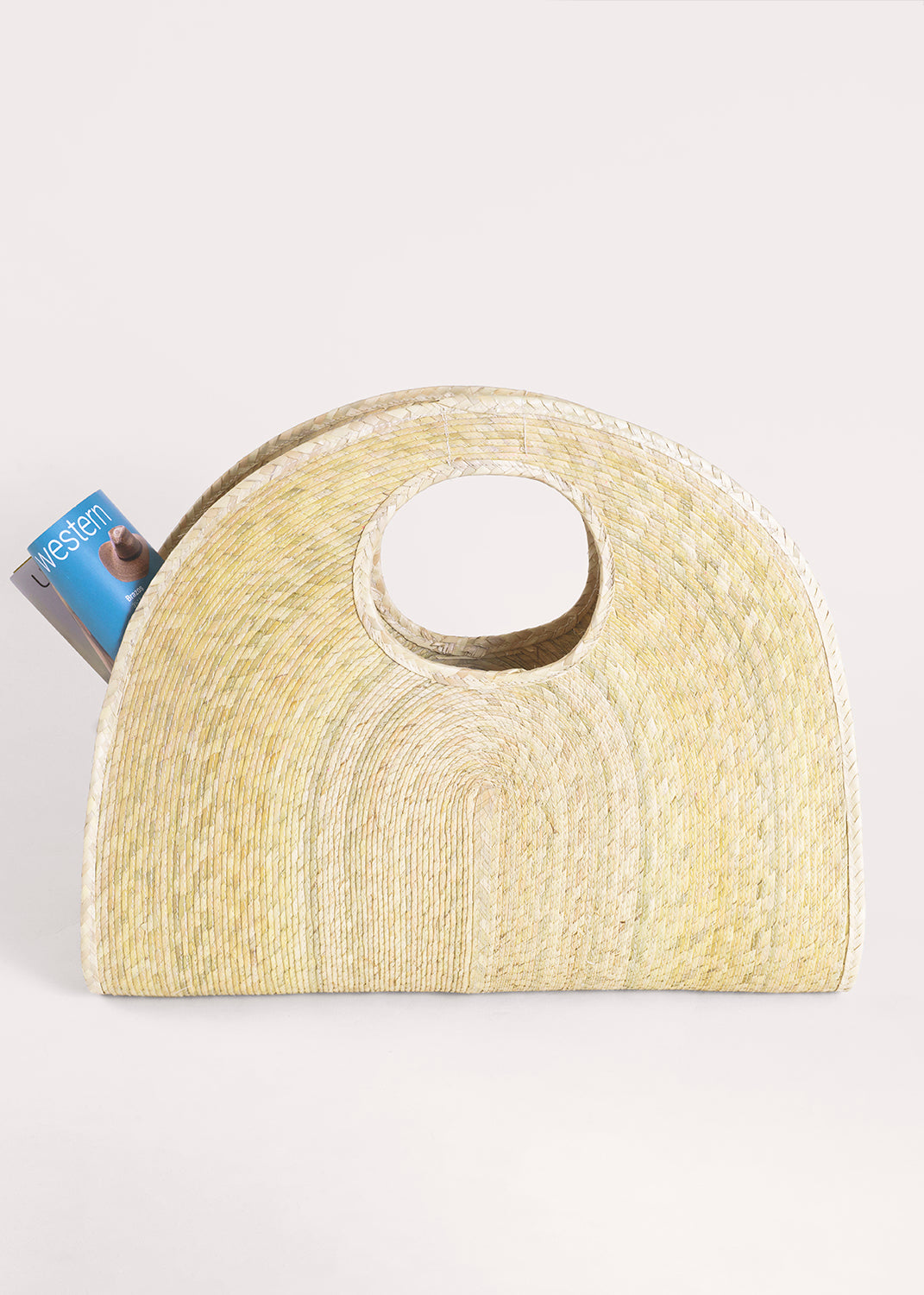 Light palm straw half-circle Concha Palm Tote with a circular handle and magazine.